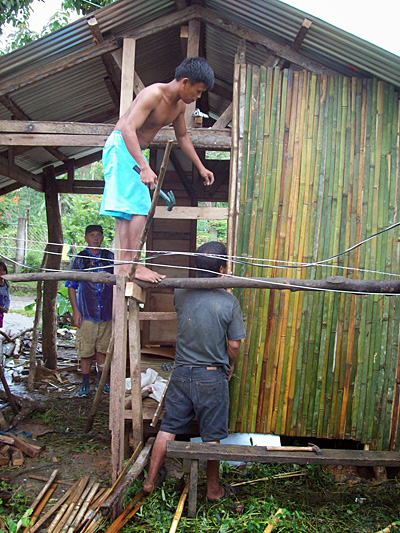 pose des lattes debmabous sur les murs d'une maison reconstruite à Tambis